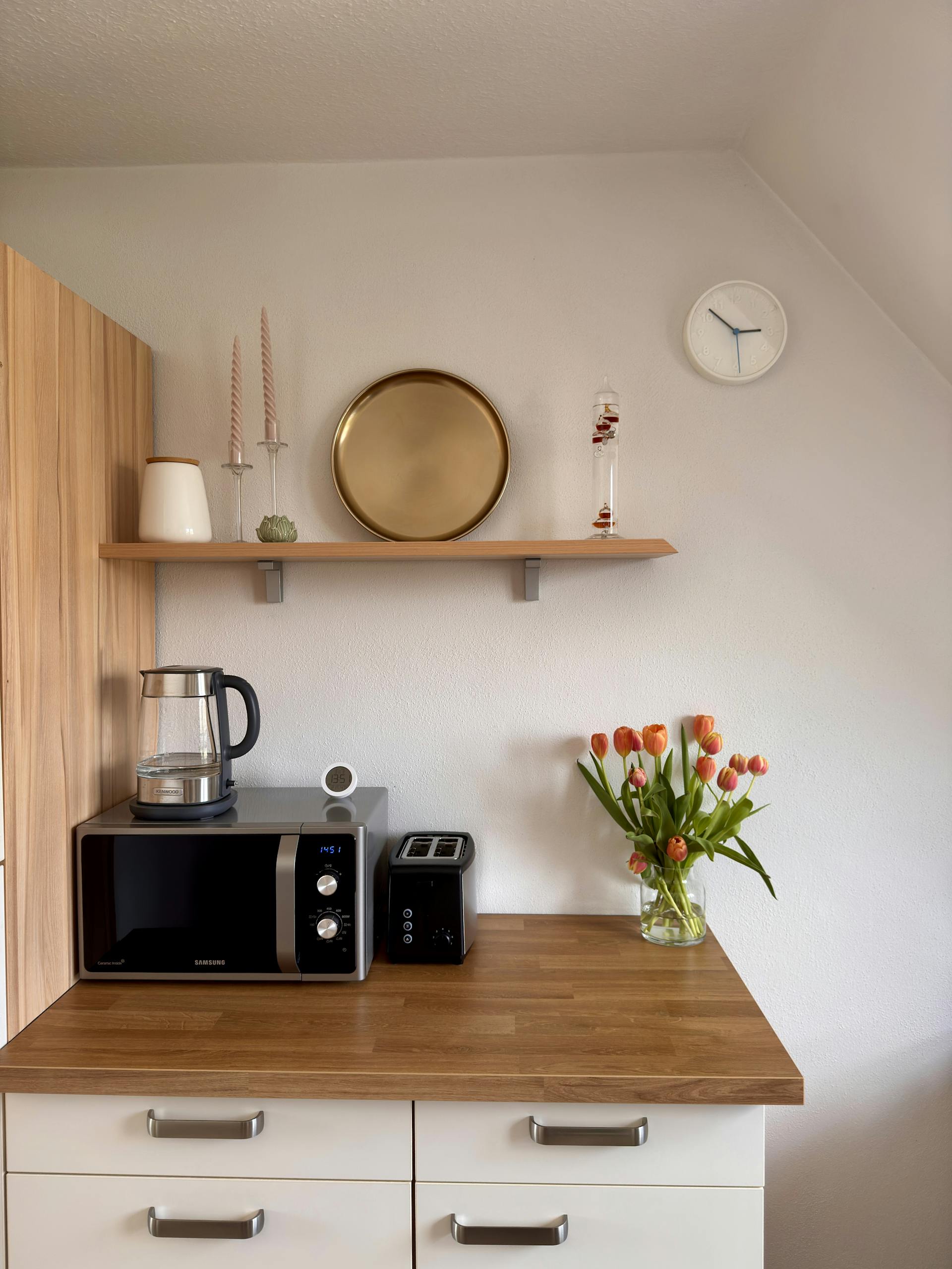 A stylish kitchen counter with tulips, toaster, and microwave on a wooden surface.